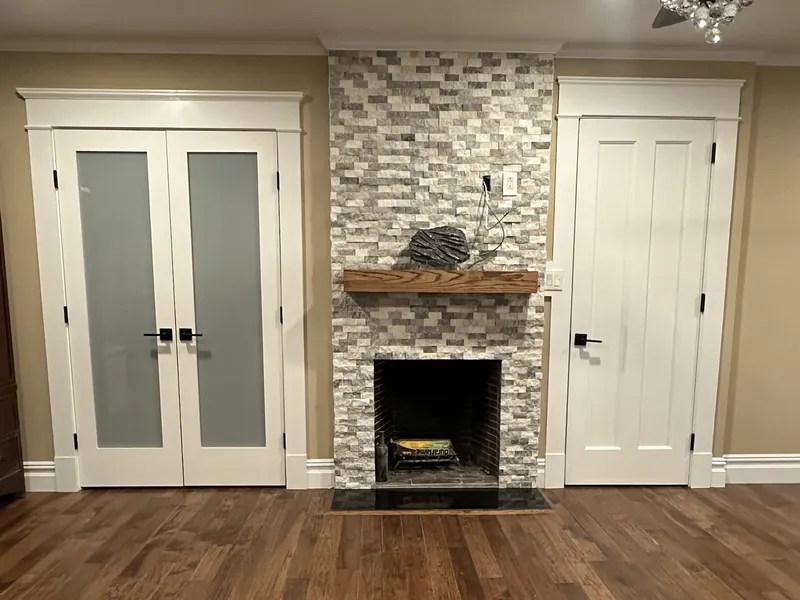 Stacked-stone fireplace with a wood mantel between white French doors, over hand-scraped hardwood floors