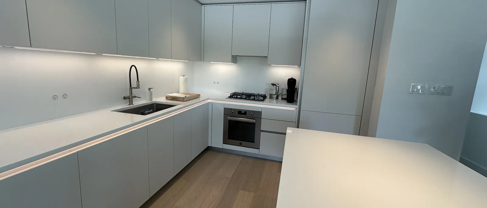 Modern white kitchen with handle-free cabinets, under-cabinet lighting, a gas cooktop and a quartz island