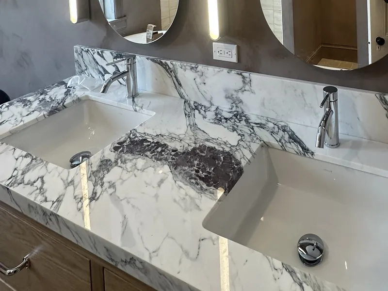 Double vanity with a purple-veined marble top, undermount sinks, oval mirrors and vertical LED lights