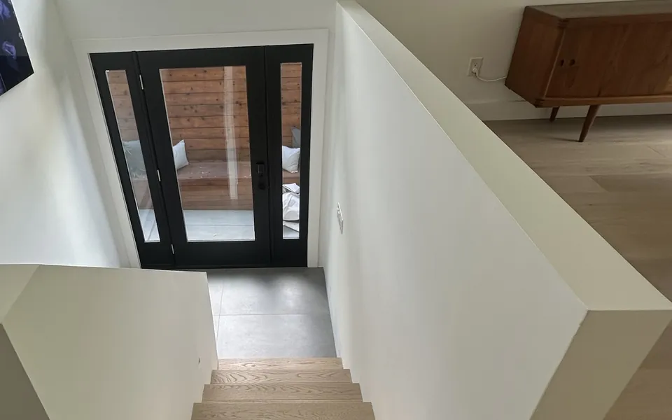 Stair hall with white walls, white oak stairs and a black-framed glass entry door